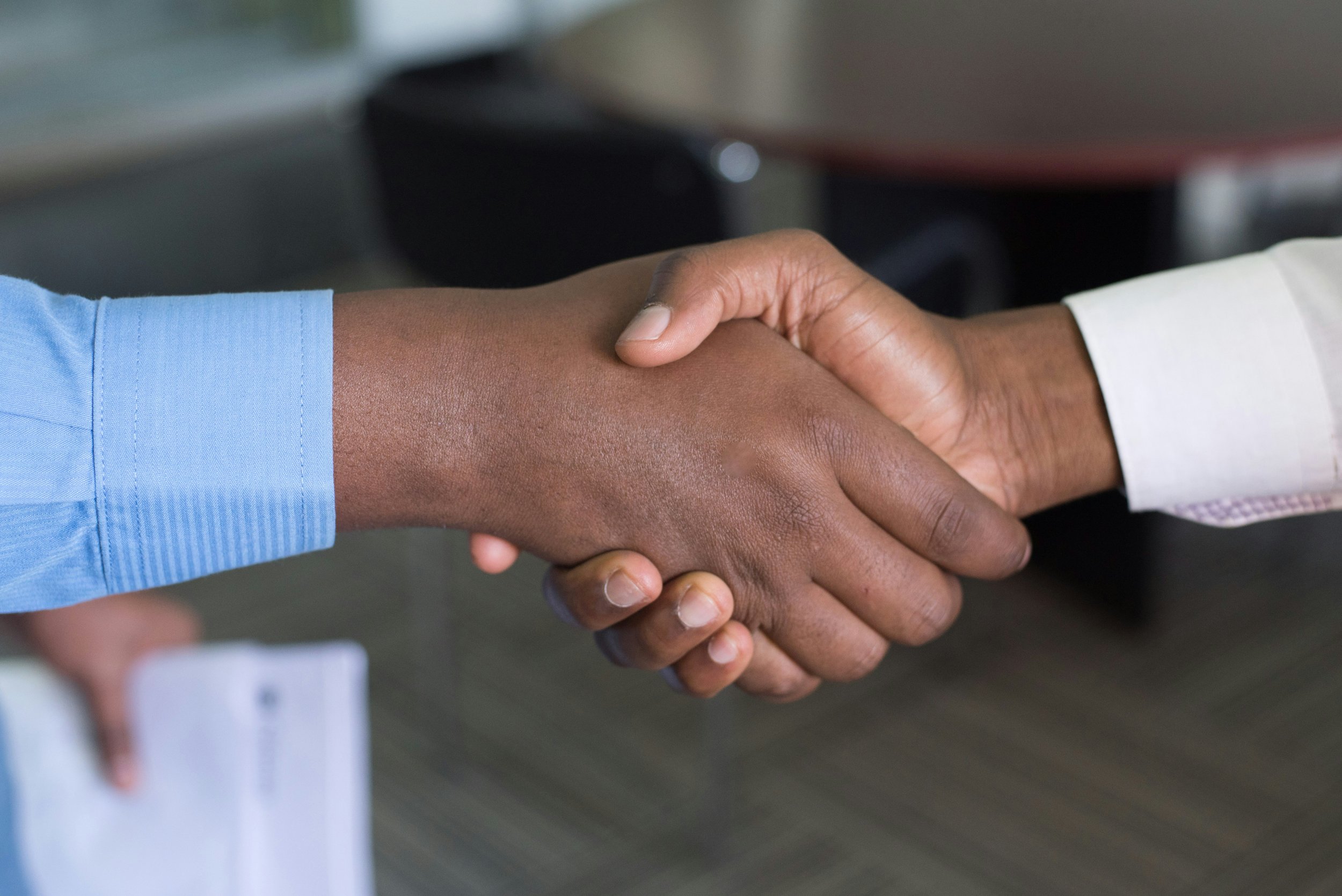 Two professionals shaking hands in a modern office setting, symbolising agreement and collaboration.