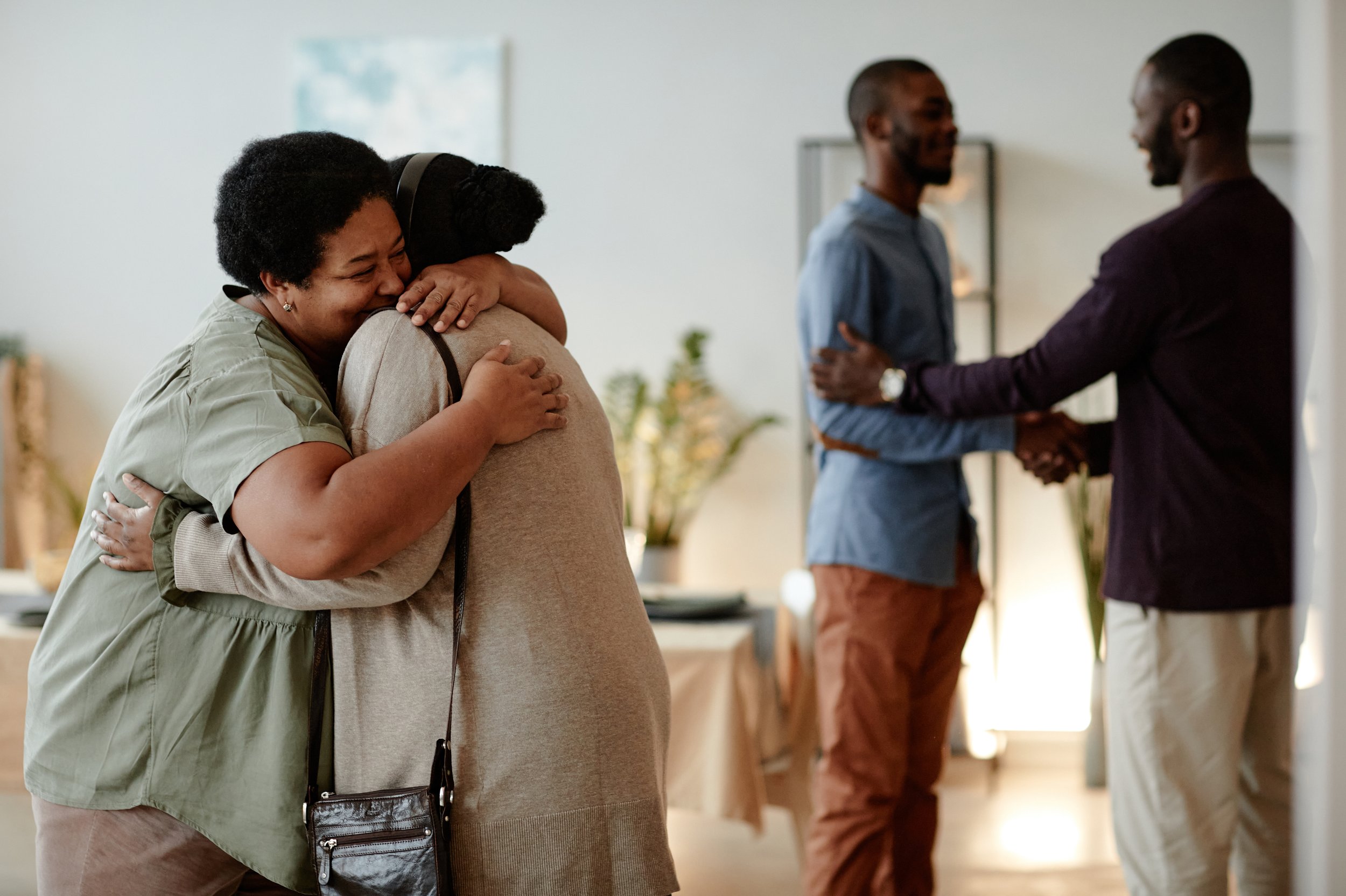 Two people hugging and two people shaking hands in a warm, indoor setting.