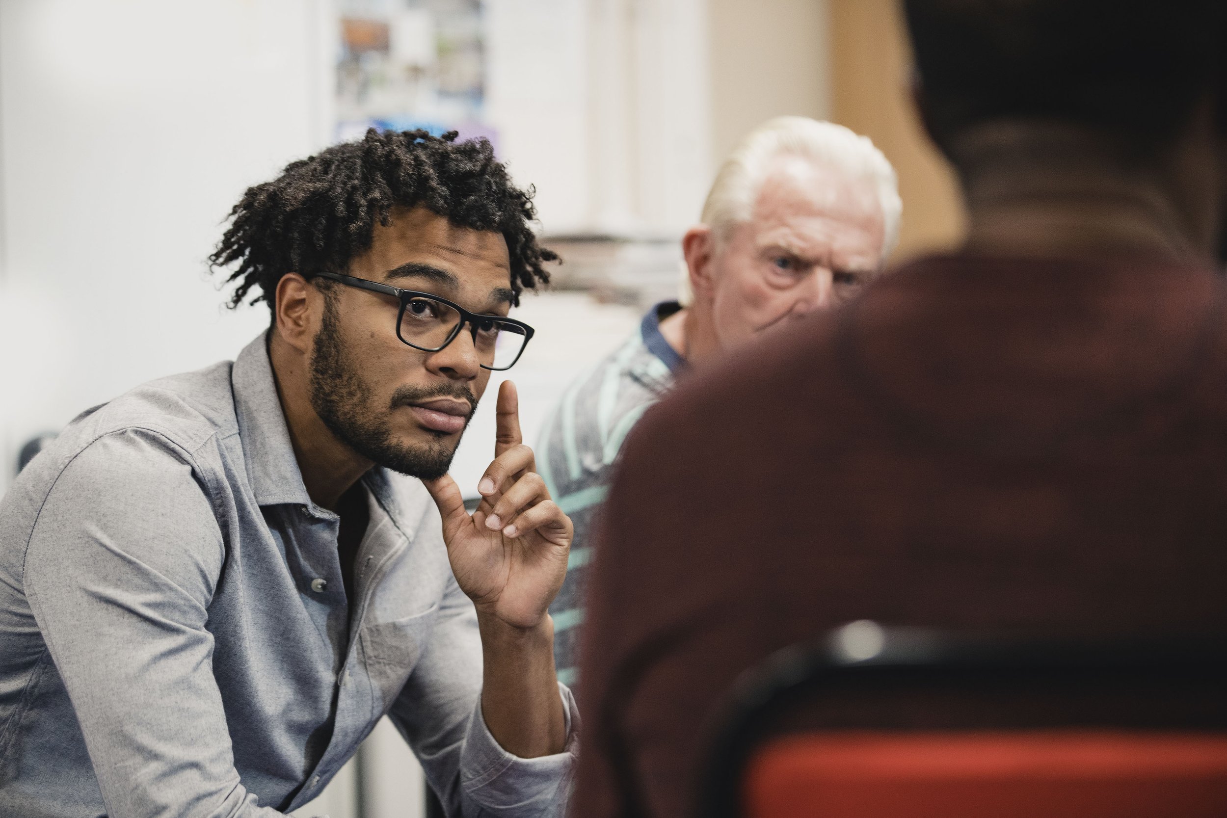 A man wearing glasses engages in conversation with another man, both appearing attentive and engaged in discussion.
