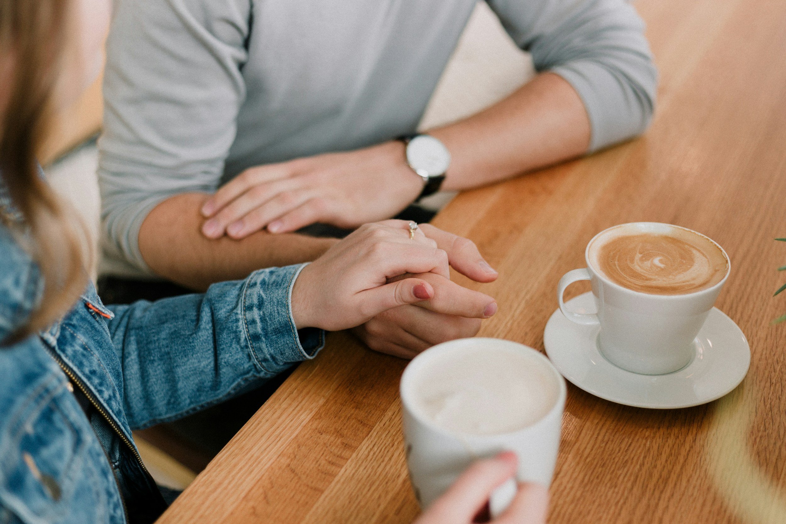 Two individuals at a table, One holding the other's hand beside over coffee cups, conveying empathy and emotional support for that person.