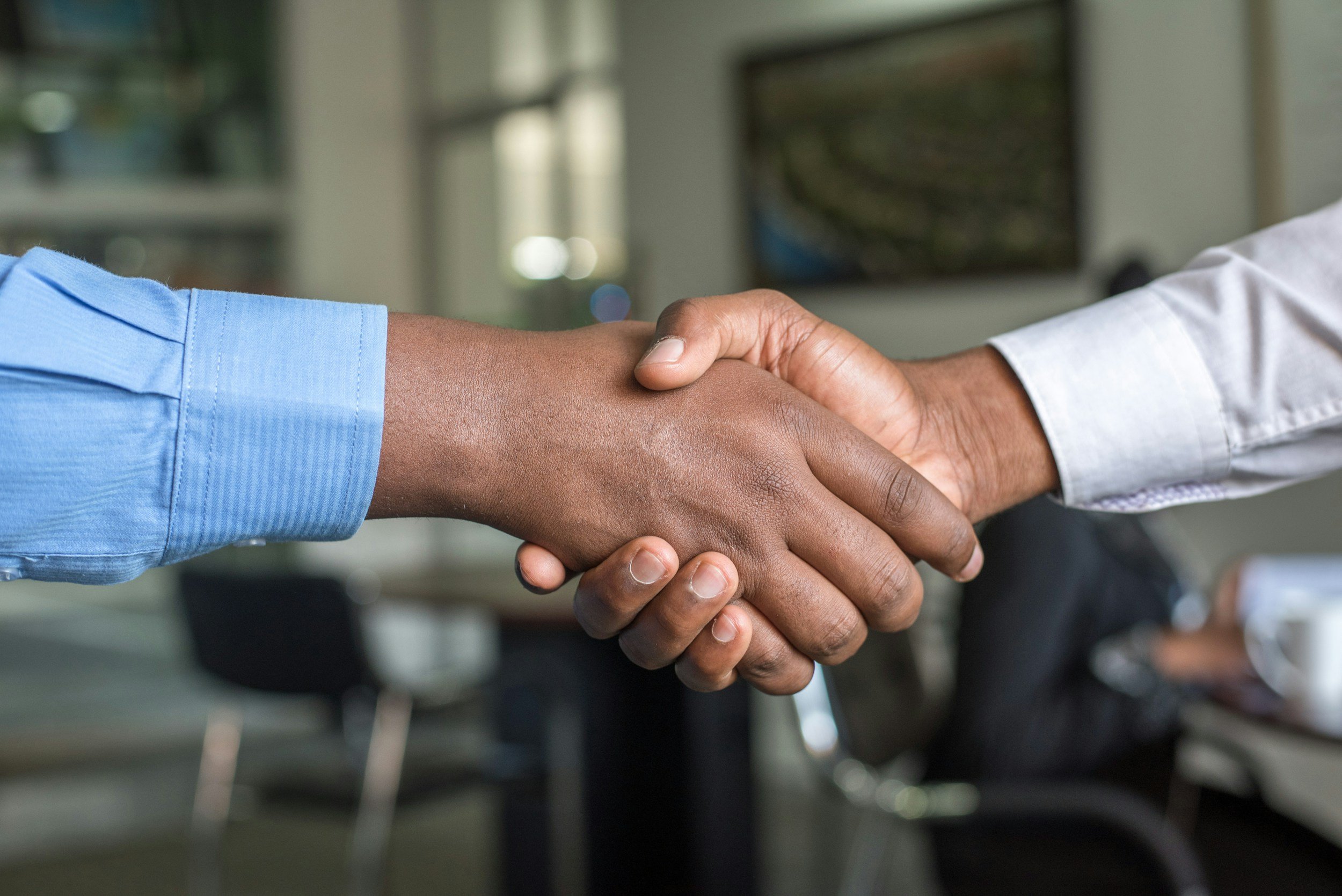Two professionals shaking hands in a modern office setting, symbolising agreement and collaboration.